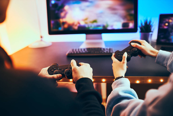 Friends playing video game at home. Gamers holding gamepads sitting at front of screen. Streamers girl and boy playing online in dark room lit by neon lights. Competition and having fun - Foto, Bild