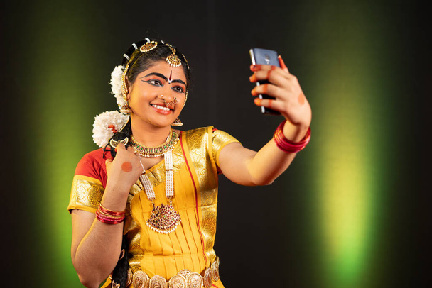 Portret shot van jong meisje in Bharatnatyam danser kostuum selfie op mobiele telefoon - concept van social media delen, hobby en technologie. - Foto, afbeelding