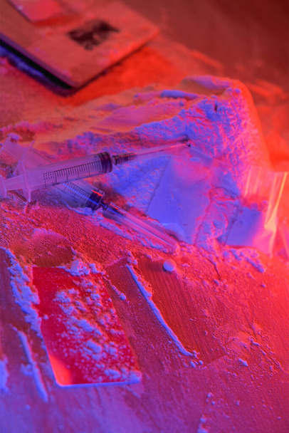 Drugs, drug dealer's house. Cocaine packaged in sachets, scales: tablets and syringes in neon light. Illegal, entry. - 写真・画像