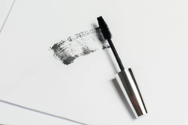 Mascara lies on a white background, and leaves a black mark showing how the brush works. Cosmetics and make-up personal care. - Фото, изображение