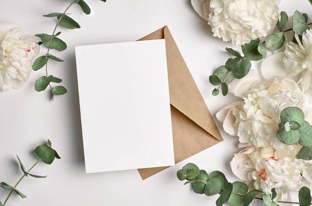Wedding invitation or greeting card mockup with envelope and white peony flowers with eucalyptus twigs on white background - Foto, immagini
