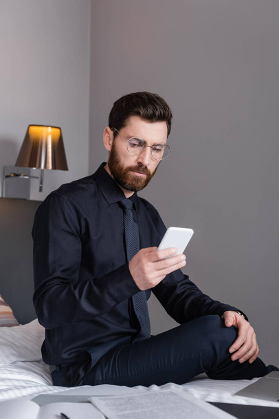 bearded man in suit and eyeglasses using smartphone in hotel  - Fotó, kép