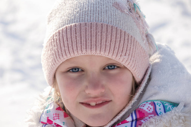 retrato de invierno de una niña de 7-8 años, primer plano, sobre el fondo de la nieve, que sonríe con la boca abierta sin dientes de leche - Foto, Imagen