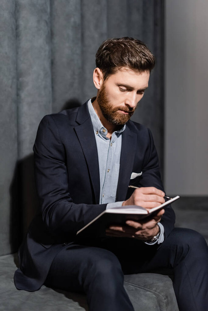 bearded businessman writing in notebook in hotel foyer  - Фото, изображение