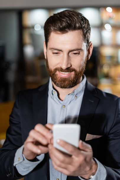 cheerful man in suit using mobile phone in hotel lobby - Photo, image