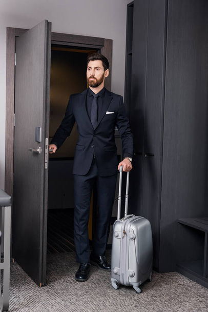 businessman in formal wear holding baggage handle and entering room in hotel - Foto, Imagem