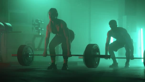 スローモーションで色鮮やかなネオンレッドとブルーのライトの男と女が重い鐘を頭の上に持ち上げます。重量のある強さとパワートレーニング。運動と強いカップルの概念 - 映像、動画