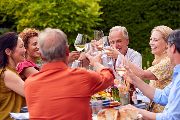 Group Of Mature Friends Talking And Making A Toast With Wine At Summer Party In Garden At Home - Foto, immagini