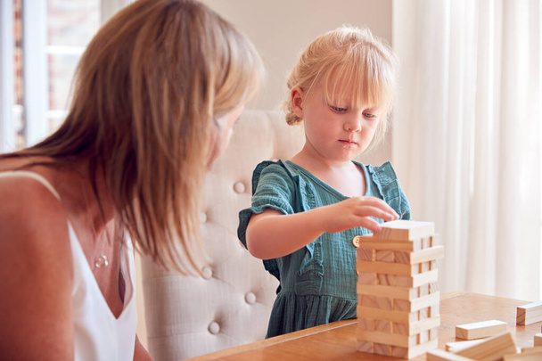 Mother And Daughter Having Fun Sitting At Table Playing Game Building Tower From Wooden Blocks - Zdjęcie, obraz