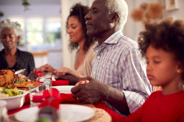 Multi Generation Family Hold Hands Around Table At Home Saying Grace Before Eating Christmas Meal - Foto, Imagen