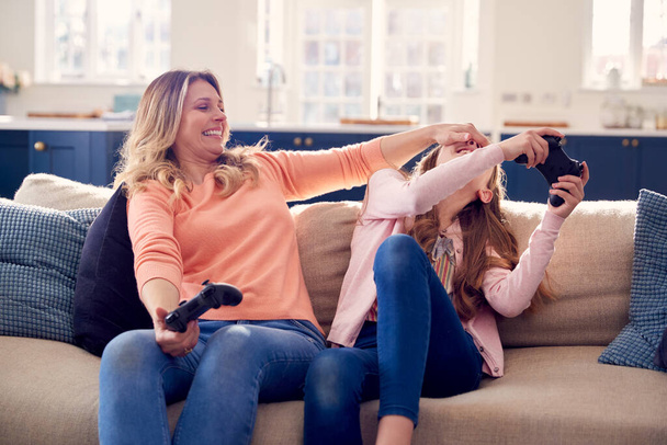 Moeder bedriegen als ze en dochter veel plezier zitten op de bank thuis spelen op Games Console - Foto, afbeelding