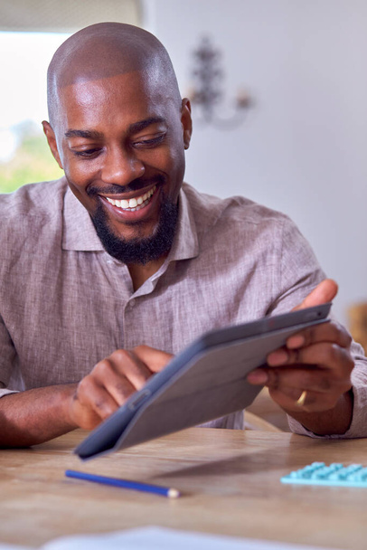 Smiling Man Sitting At Table At Home Using Digital Tablet - Foto, Bild