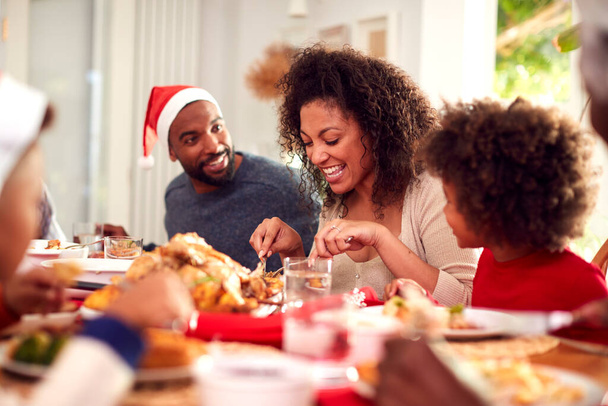 Family In Paper Hats Enjoying Eating Christmas Meal At Home Together - Foto, Imagem