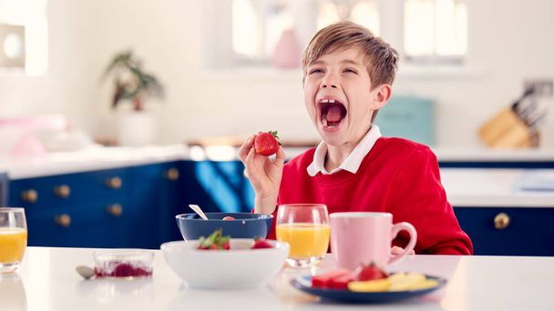 Laughing Boy Wearing School Uniform In Kitchen Eating Healthy Breakfast With Fresh Strawberry - Foto, Imagem