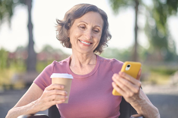 Eine Frau mit einem Handy in der Hand sieht glücklich und lächelnd aus - Foto, Bild