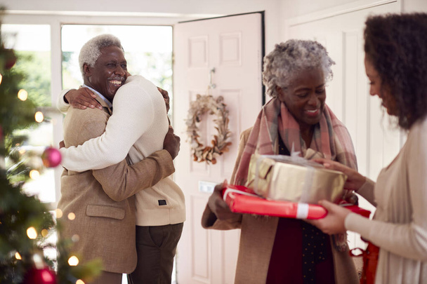 Adult Children Greeting Senior Parents As They Arrive With Presents To Celebrate Christmas - Фото, изображение
