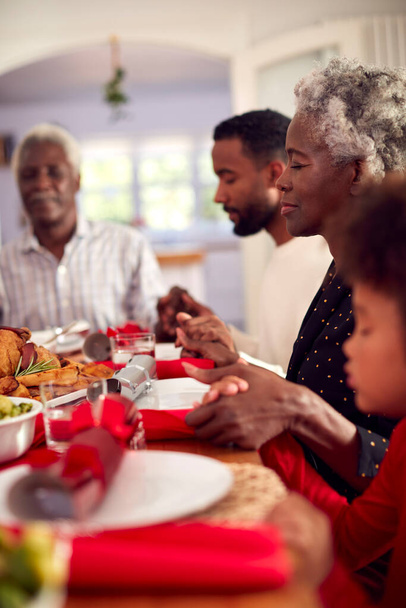 Multi Generation Family Hold Hands Around Table At Home Saying Grace Before Eating Christmas Meal - Photo, image