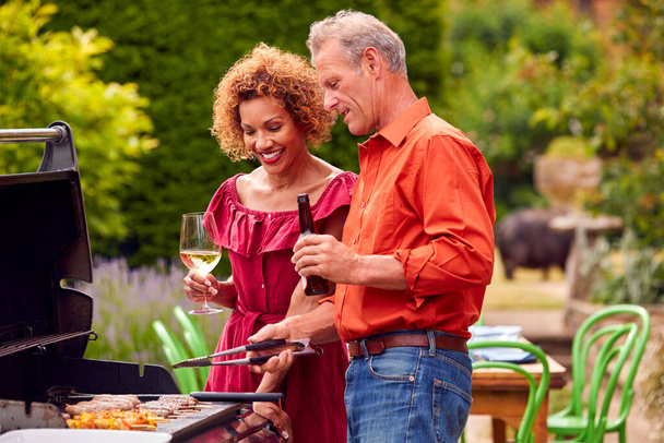 Senior Couple Cooking Outdoor Barbeque And Drinking Wine And Beer At Home - Фото, изображение