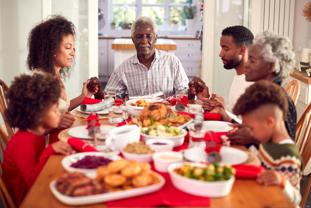Multi Generation Family Hold Hands Around Table At Home Saying Grace Before Eating Christmas Meal - Foto, Imagen