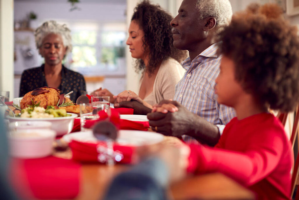 Multi Generación de las manos de la familia alrededor de la mesa en casa diciendo gracia antes de comer comida de Navidad - Foto, Imagen