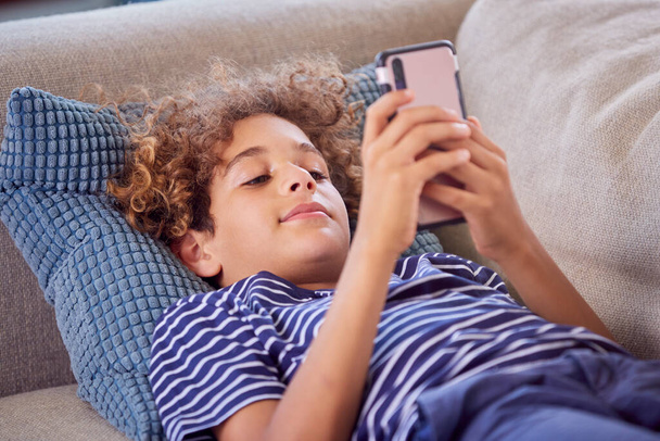 Boy Lying On Sofa At Home Playing Online Game With Mobile Phone - Valokuva, kuva