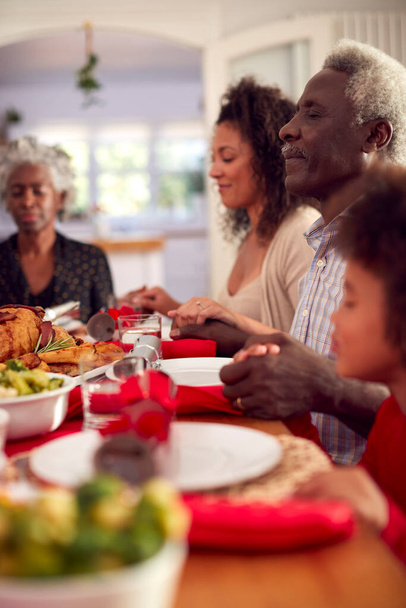 Multi Generation Οικογένεια κρατήστε τα χέρια γύρω από το τραπέζι στο σπίτι λέγοντας προσευχή πριν από το φαγητό χριστουγεννιάτικο γεύμα - Φωτογραφία, εικόνα