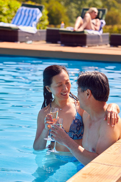Loving Mature Couple Relaxing In Swimming Pool On Summer Vacation Celebrating Drinking Champagne - Photo, image