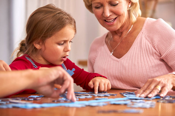 Granddaughter With Grandmother Sitting Around Table At Home Doing Jigsaw Puzzle Together - Foto, Imagem