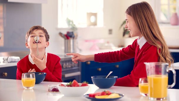 Brother And Sister Wearing School Uniform In Kitchen Have Fun Hanging Spoon From Nose At Breakfast - Foto, Imagem
