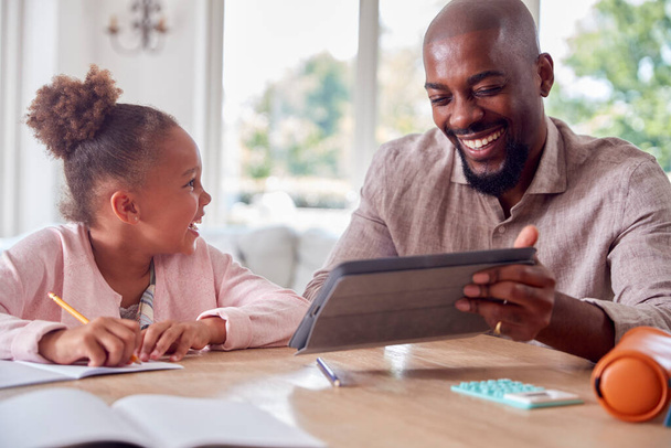 Father Helping Daughter With Home Schooling Sitting At Table With Digital Tablet - Foto, imagen