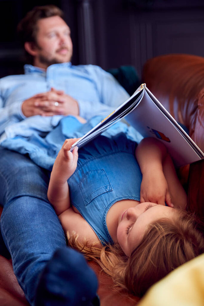 Father And Daughter Lying On Sofa At Home As Girl Reads Book - Fotó, kép