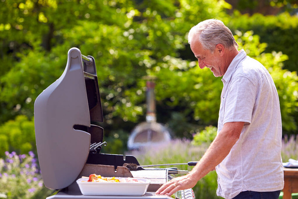 Senior Man Cooking Food On Outdoor Barbeque At Home - Foto, imagen