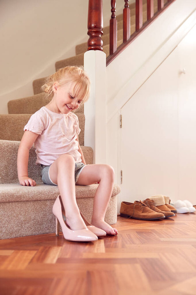 Young Girl Sitting On Stairs Dressing Up And Putting On Mother's Shoes - Foto, imagen