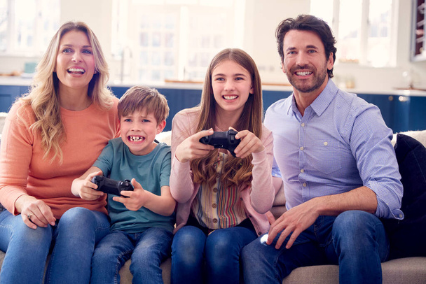 Parents Having Fun Sitting On Sofa With Children At Home Playing On Games Console - Zdjęcie, obraz