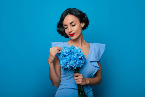 Women's day. St. Valentine's day. Close up portrait of elegant fashionable smiling woman in dress with bunch of flowers in hands isolated on blue background - Photo, image