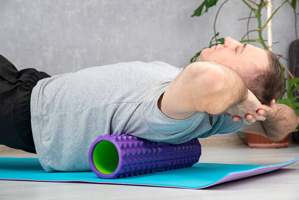 Людина робить міофасциальне вивільнення гіпер-гнучких м'язів спини з масажним пінним валиком. Самомасаж спини
 - Фото, зображення
