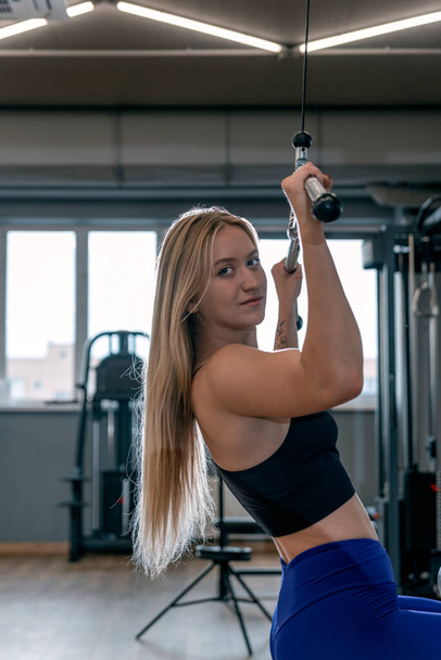 Healthy beautyful girl with sports figure trains in the gym. Back muscle training. Upper block thrust - Valokuva, kuva