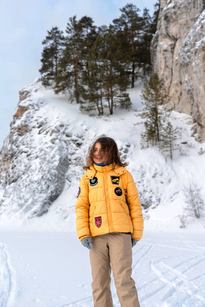 happy smiling young woman in yellow jacket walking in winter by rocks covered snow, hiking in mountains outdoors activity active lifestyle, beauty in nature positive emotions - Foto, Bild