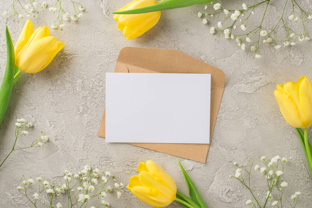 Top view photo of woman's day composition craft paper envelope and paper sheet yellow tulips and white gypsophila on isolated textured grey concrete background with copyspace - Photo, Image