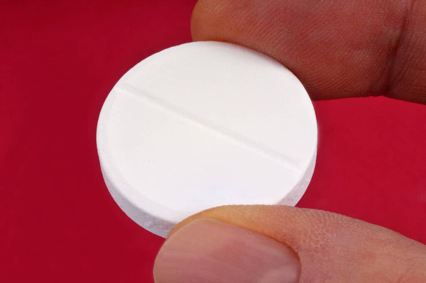 Poremainen aspiriini pilleri pidetään kädessä lähikuva punaisella taustalla  - Valokuva, kuva