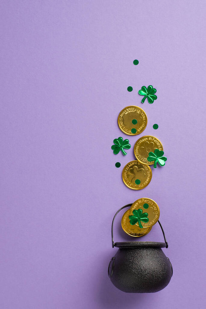 Top view vertical photo of st patricks day decorations shamrocks confetti and gold coins flying out of pot on isolated pastel violet background with copyspace - Photo, Image