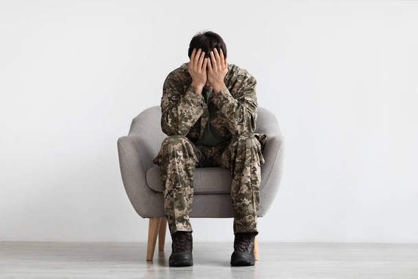 Homem infeliz em camuflagem sentado na cadeira de braço, espaço de cópia - Foto, Imagem