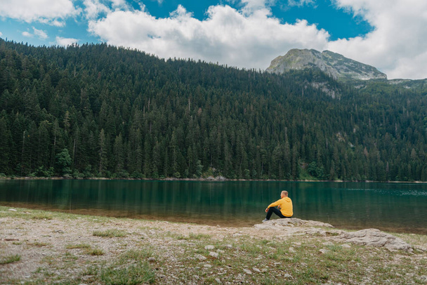 Traveler Man relaxing meditation with serene view mountains and lake landscape. Travel Lifestyle hiking concept summer vacations outdoor. Guy standing near the mountain Lake. A lonely man looks ahead - Fotoğraf, Görsel