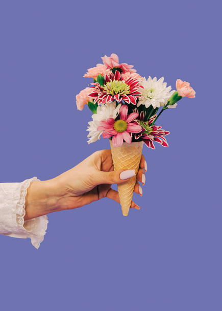 Female hand holding Ice cream waffle cornet with pastel pink roses and other various flowers over very peri background. Valentines or woman's day background. Nature Trendy Design. Creative idea. - Photo, Image