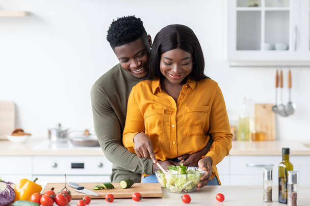 彼らは台所で一緒に昼食を調理しながらロマンチックな黒男はガールフレンドを受け入れる, - 写真・画像