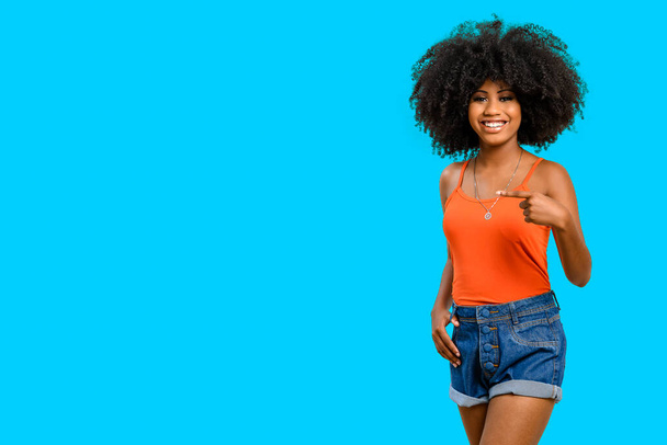 усміхнена темношкіра молода жінка вказує палець на простір ліворуч від зображення, ізольований на синьому фоні
. - Фото, зображення