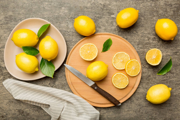 Top view with copy space for fresh and ripe lemons on cutting board. Healthy food background. Elegant background of lemon and lemon slices with squeezer and knife colored background. - Foto, Bild