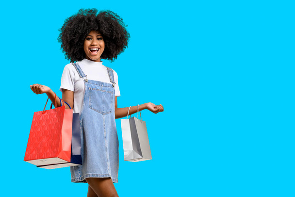 portrait of a smiling young brunette skin woman she holds shopping bags, isolated on blue background. - Foto, afbeelding