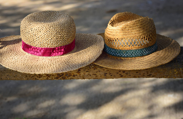 Two old straw hats, one for a woman and one for a man, lie side by side on a wooden bench in the shade, with space for text underneath - Foto, Imagem
