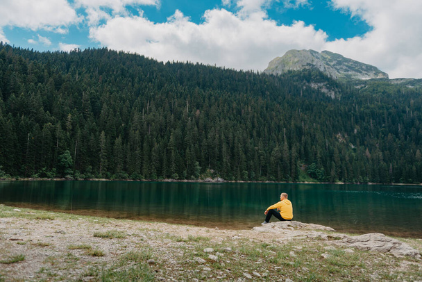 Traveler Man relaxing meditation with serene view mountains and lake landscape. Travel Lifestyle hiking concept summer vacations outdoor. Guy standing near the mountain Lake. A lonely man looks ahead - Photo, Image